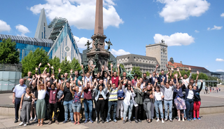 Teilnehmende der Summer School an der Universität Leipzig stehen am Augustusplatz Leipzig und strecken ihre Hände in die Höhe.